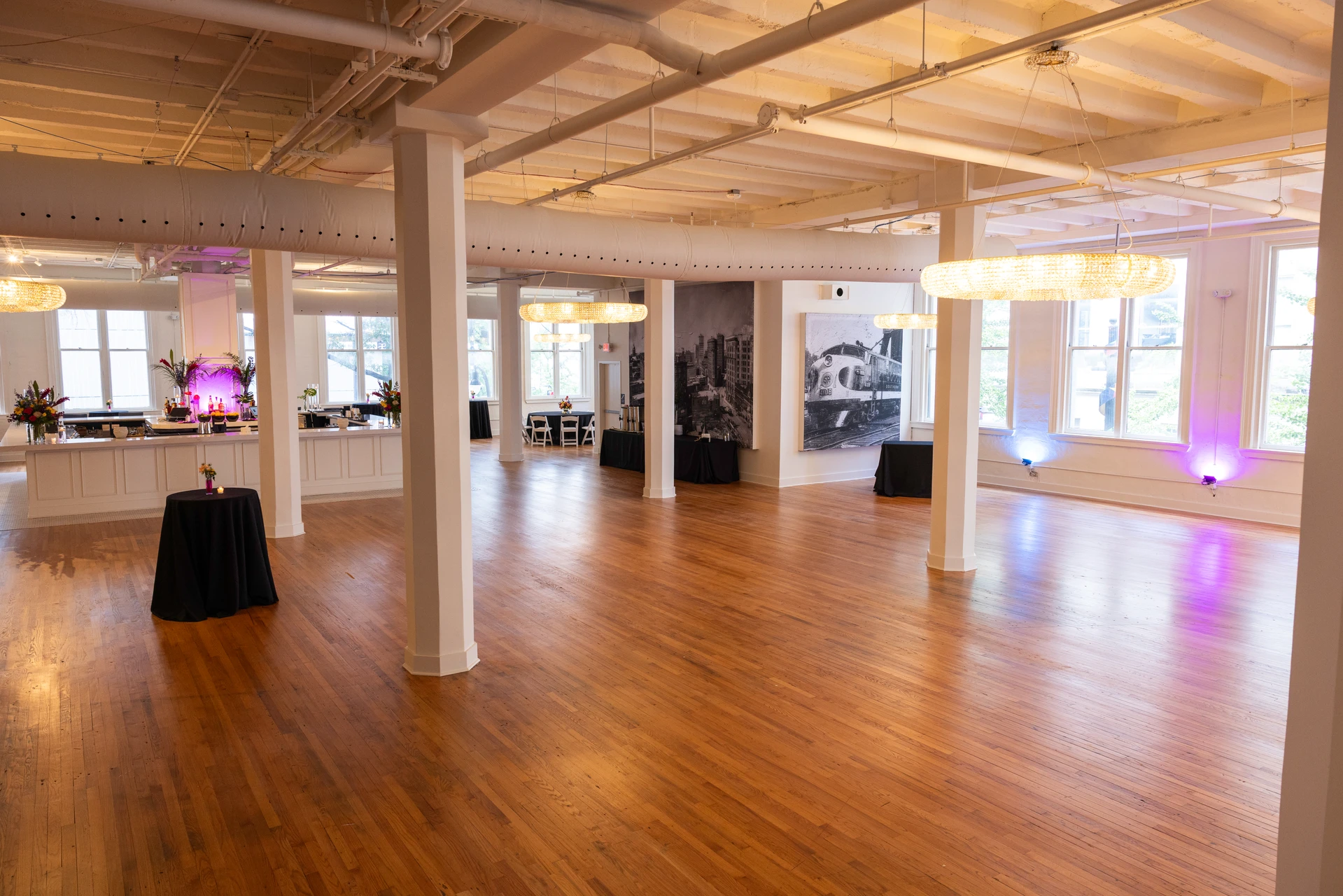 Grand Ballroom with white columns, crystal ring chandeliers, tall windows and an open wood floor.