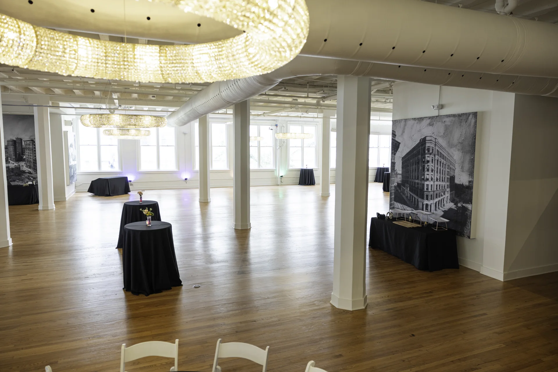 A diagonal view across Grand Ballroom with a crystal chandelier, white columns, tall windows and a large building artwork.