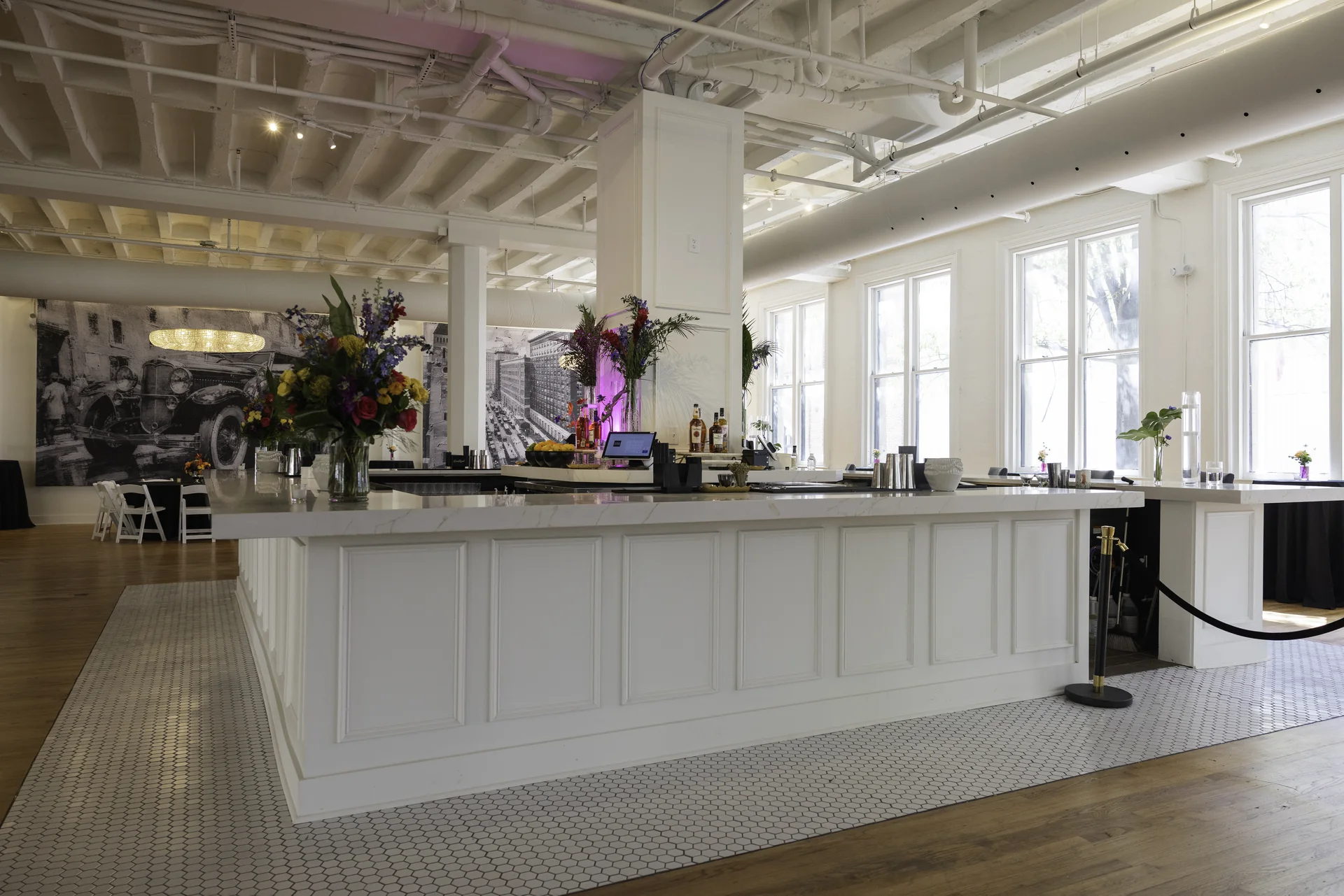 The front of Grand Ballroom’s white paneled bar with floral arrangements and daylight through the windows.
