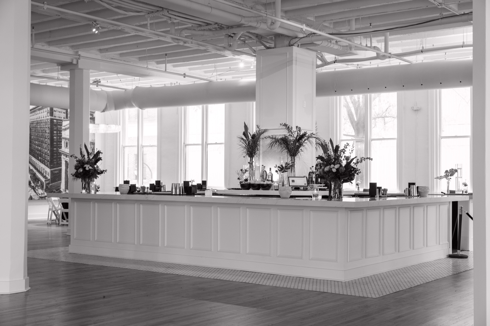 The Grand Ballroom bar with a white paneled counter, floral arrangements and tall windows.